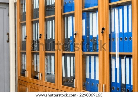 Wooden and glass office binders cabinet that hold a large number of binders in an office to keep and store the data of the company, soft and selective focus on document binders.