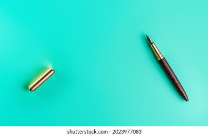 Wooden and gold fountain ink pen, opened, cap on the left, blue green background top down view, space for text middle