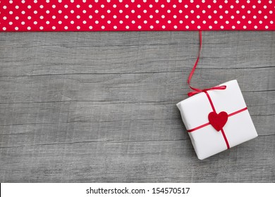 Wooden grey background with a present wrapped in paper with a red heart for christmas, valentine, mother's day or anniversary - for a greeting card - Powered by Shutterstock