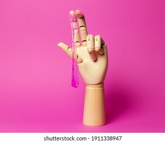 Wooden hand with dripping pink liquid paste pink background. Hair removal and sex concept.