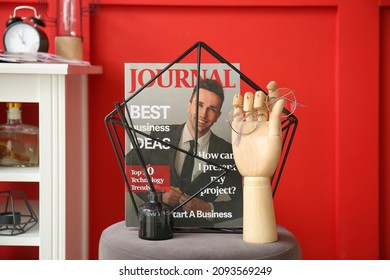 Wooden Hand With Eyeglasses And Magazine On Pouf Near Color Wall