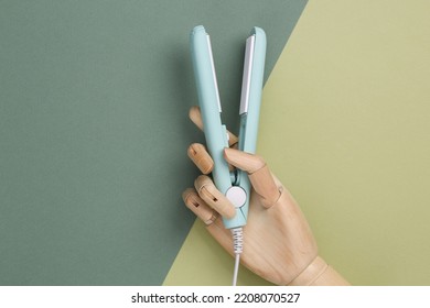 Wooden Hand Holding Mini Hair Straightener On Green Background. Top View