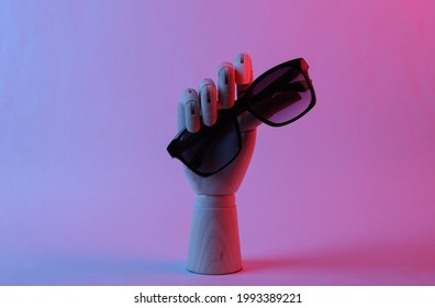 Wooden hand holding sunglasses in pink blue gradient neon light