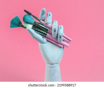 Wooden Hand Holds Makeup Brushes On Pink Background