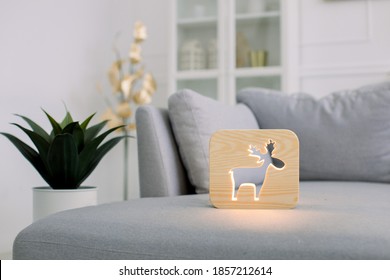 Wooden Hand Made Accessories. Wooden Night Lamp With Deer Picture, On Gray Cozy Soft Sofa, At Stylish Light Home Living Room Interior. Home Decor And Lamps.