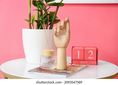 Wooden Hand With Magazine And Decor On Table Near Color Wall