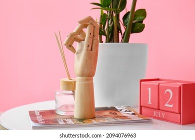 Wooden Hand With Magazine And Decor On Table Near Color Wall