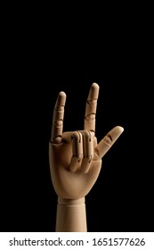 The wooden hand of a mannequin for drawing shows rock n roll sign, rocker gesture on a black background. Side view. Art model for drawing. Part of the body - hand, brush.