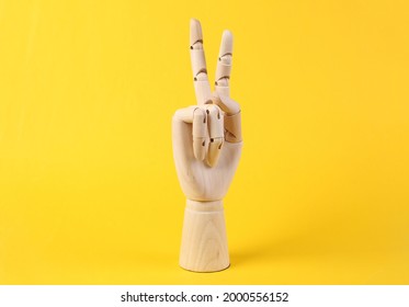 Wooden hand shows v gesture on yellow background 