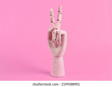 Wooden hand shows v gesture on pink background 