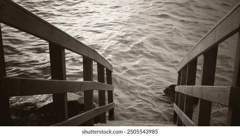 A wooden handrail, in gray tones, extends to the edge of a pier, plunging into the equally gray seawater. The black and white scene conveys a sense of calm and simplicity. - Powered by Shutterstock