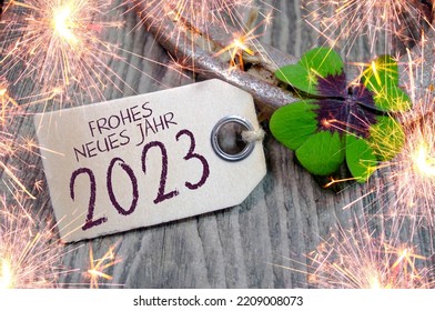 Wooden hang tag and slate with four leaf clover and sparklers with the german words for happy new year - frohes neues jahr 2023 on wooden weathered background	