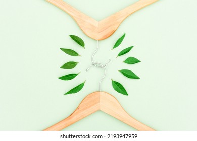 Wooden Hangers With Green Leaves Over Mint Background As A Symbol Of Conscious Consumerism, Slow Fashion And Environmentally Friendly Fashion. Reuse, Recycling And Upcycling Clothes. Green Shopping