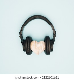 Wooden heart with black headphones on pastel blue background. Feelings and emotions. Music and sound. Flat lay.