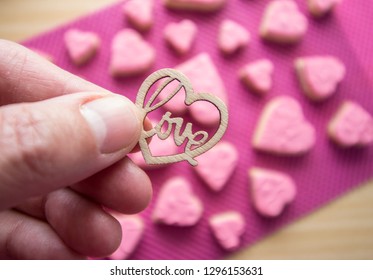 Wooden heart with the word love inside. Background of pink cookies. Valentine's Day, Mother's Day. Hand. 