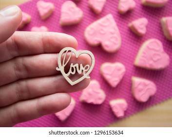 Wooden heart with the word love inside. Background of pink cookies. Valentine's Day, Mother's Day. Hand. 