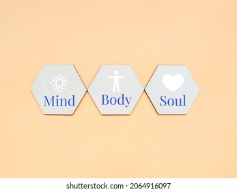 Wooden Hexagon With Icon Of Mind, Body And Soul Against Dark Yellow Background.