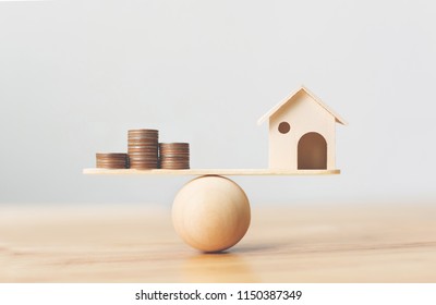 Wooden home and money coins stack on wood scale. Property investment and house mortgage financial real estate concept