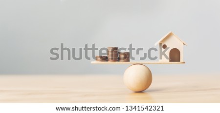 Wooden home and money coins stack on wood scale. Property investment and house mortgage financial real estate concept