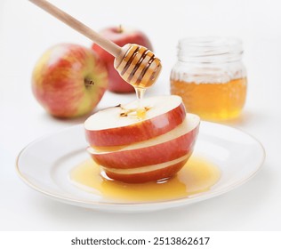 A wooden honey dipper drips honey onto sliced apples. The apples are arranged in a stack on a white plate, with a jar of honey and two whole apples in the background. - Powered by Shutterstock