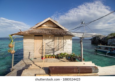 Wooden House Above The Water With Parabolic Satellite And Flower Pots In Front Of The House And Ocean Behind The House