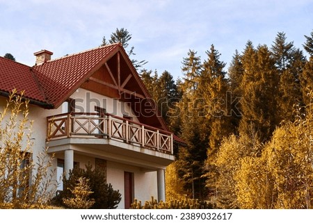 Wooden house in beautiful nature. Mountain style house. Pretty landscape with modern wooden house surrounded by trees with colorful foliage and mountains. Runaway chalet cabin in the forest.