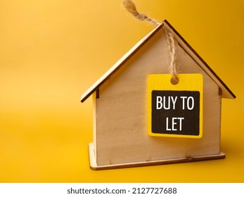 Wooden House And Wooden Board With Text BUY TO LET On A Yellow Background.