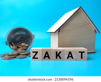 Wooden House And Coins With Text ZAKAT On A Blue Background.