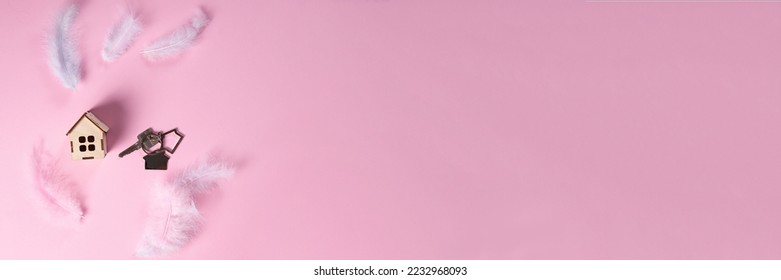 A wooden house and the keys on a pink pastel background with feathers.Long banner. The concept of an easy loan, mortgage, insurance, copy space for your advertising. Flat lay. - Shutterstock ID 2232968093