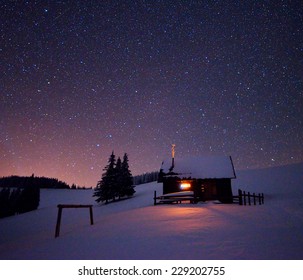 Wooden House With A Light In The Window. Night Landscape In Winter