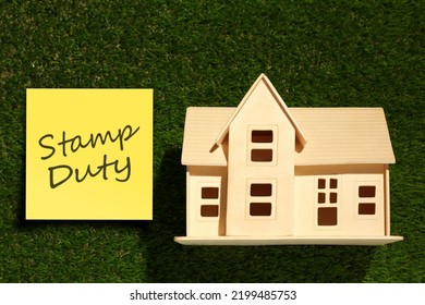 Wooden House Model Ans Sticky Note With Text Stamp Duty On Green Grass, Top View