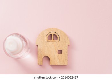 Wooden house model with the bottle of alcohol gel on pink background for healthcare and sanitary items at home on the epidemic situation concept