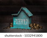 Wooden house model with coins next to it with conceptual text. Freehold