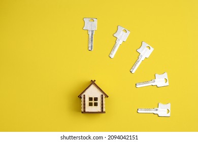 Wooden House Model And House Keys On A Colored Background. Real Estate Buying And Selling Concept. Top View, Flat Lay.