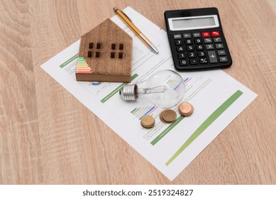 Wooden house model, light bulb, coins, and calculator on energy efficiency documents on wooden table, home energy savings concept - Powered by Shutterstock