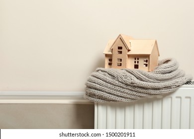 Wooden house model and scarf on radiator indoors, space for text. Heating efficiency - Shutterstock ID 1500201911