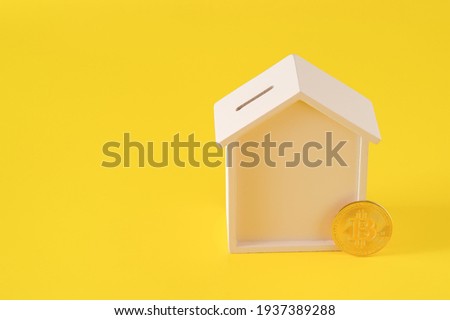 Wooden house moneybox and bitcoin on yellow background. E-commerce concept, purchase of real estate for cryptocurrency concept, copy space for text