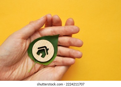 A Wooden House On A Leaf Of A Plant In The Hands Of A Man. A Symbol Of Environmentally Friendly Housing