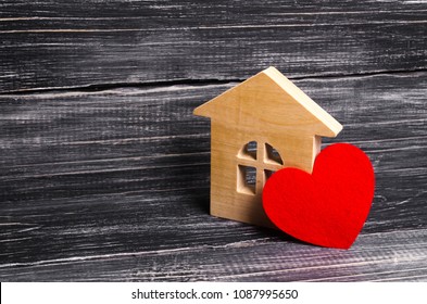 Wooden house with a red heart on a dark wooden background. A house for lovers, a honeymoon. Purchase your own affordable housing for young families. Planning family and offspring