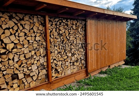 wooden house with a roof and windows made of planks embedded in leveled split wood for heating in a cottage or house. in niche are flower beds with red blooming geraniums in autumn alpine landscape