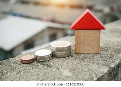Wooden house and stacks of coins standing next ,Little wooden house made of toy blocks on beautiful blue and city background ,Real estate concept, Choose your best deal, saving money for real estate