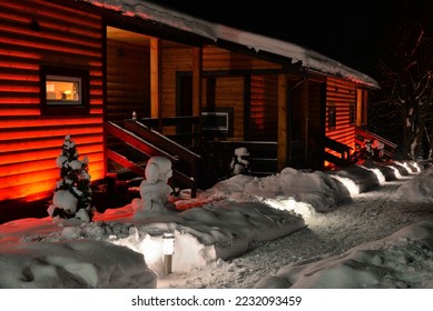 Wooden house with terrace with red illumination in winter evening  in village 