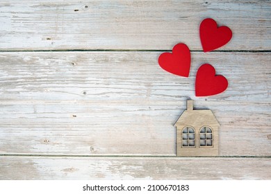 Wooden house with three red hearts on a wooden background. Love nest, love relationships. Buying a house with a young family. Affordable housing. banner. Family psychology, strong relations.  space - Shutterstock ID 2100670183