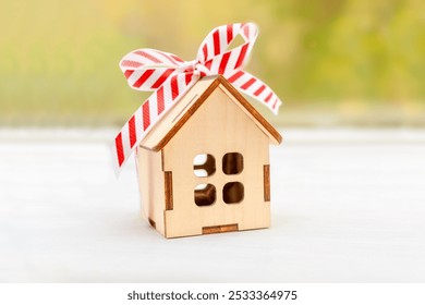 Wooden house with a tied bow made of white red wrapping ribbon on table near window close-up, background. Gift, present, buying a new house, mortgage, real estate concept. - Powered by Shutterstock