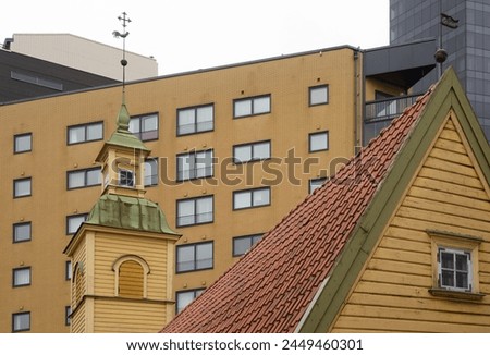 wooden house with a tiled roof and a turret with a weather vane against the background of modern buildings in Tallinn, Estonia 

 