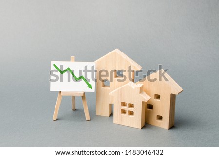Wooden houses and an easel arrow down. The fall of the real estate market. concept of value or cost decrease. low liquidity and attractiveness. cheap rent. Reduced demand and market stagnation.