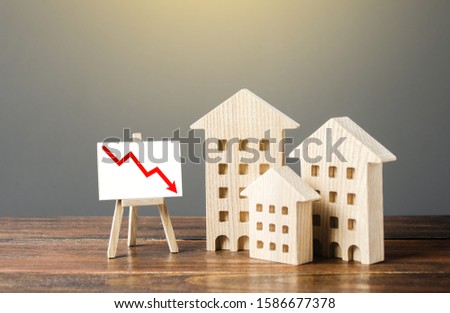 Wooden houses residential buildings and an easel with a red down arrow. Fall of real estate market. Value cost decrease. Bad liquidity attractiveness. Cheap rent. Reduced demand, recession. Low sales