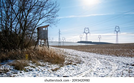 Wooden Hunt tower near the agricultural field in the winter. Huntsman high seat with High voltage power lines and power pylons.