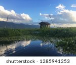 Wooden hut in field with blue cloudy sky near water pond river in Myanmar Inle Lake region