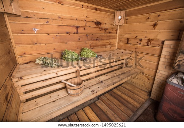 The wooden interior of the\
Russian banya with benches, bucket and bath brooms; tradition\
concept.